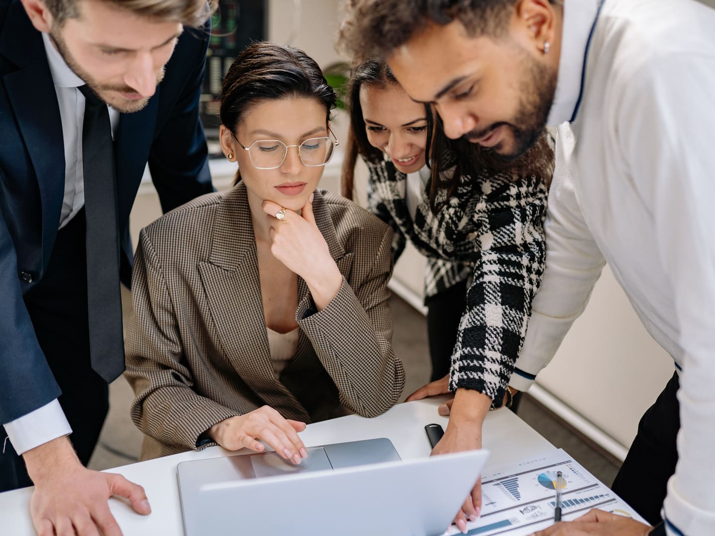 Four colleagues gathered around a laptop and reviewing information together.